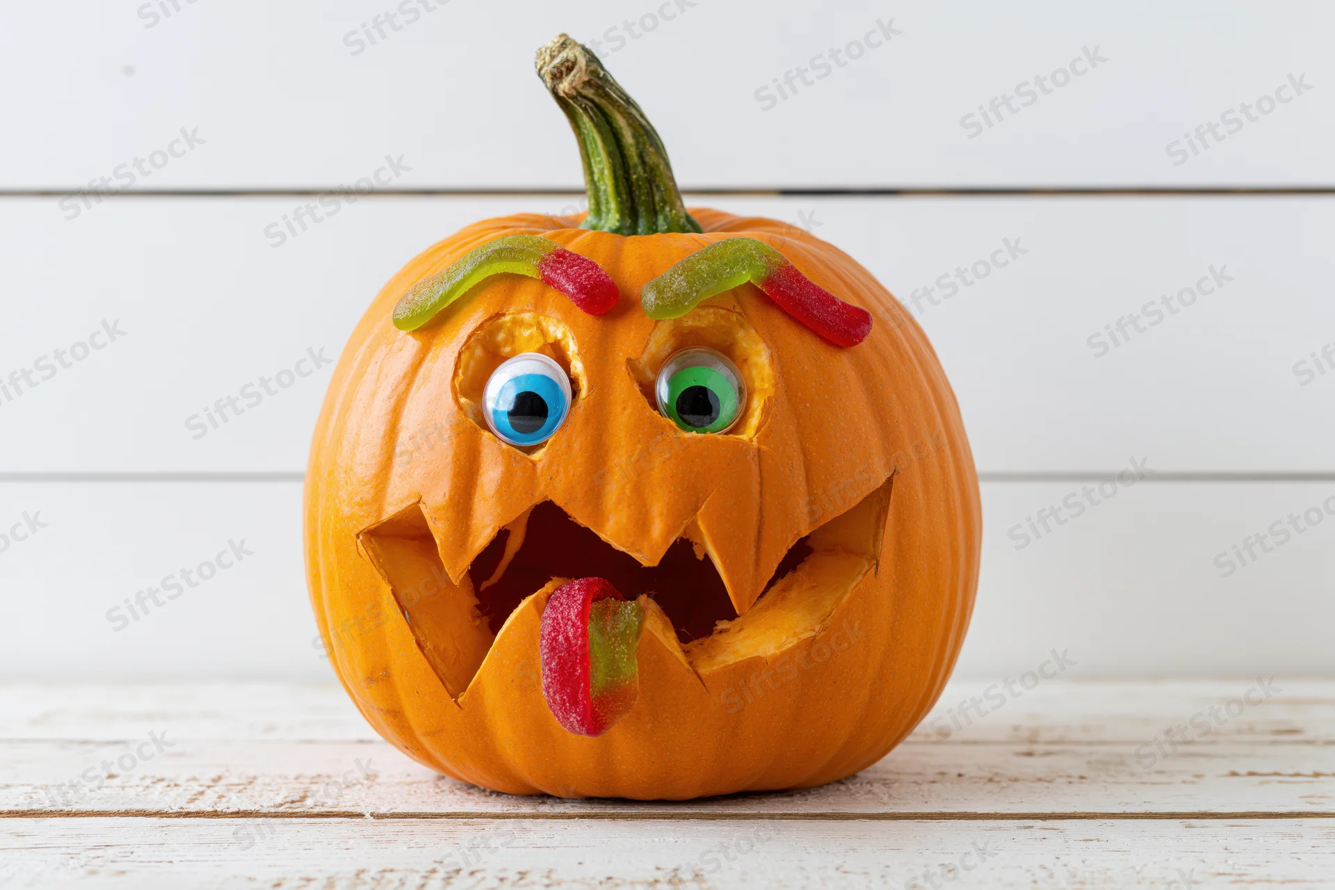 Carved pumpkin with gummy worm candies for halloween decoration on white wooden surface