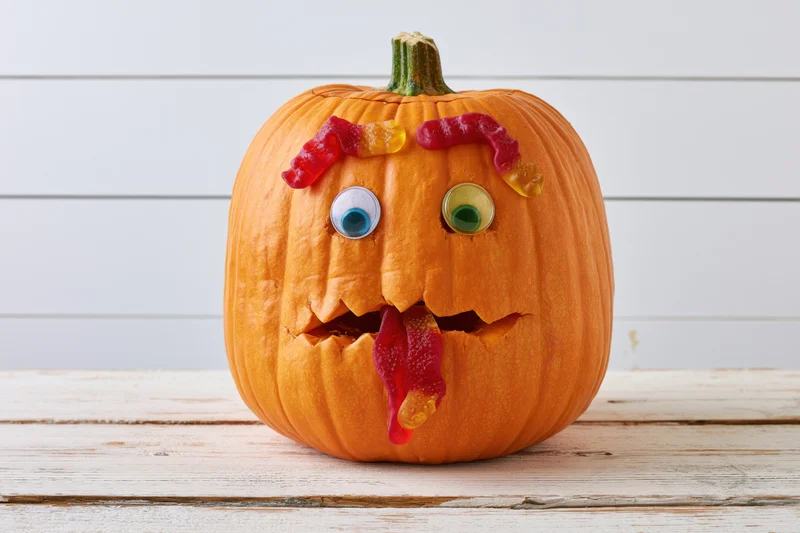 Carved pumpkin with gummy worm candies forming a face on a wooden table