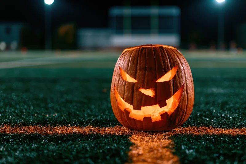Carved jack-o-lantern glowing on artificial turf at night on a sports field