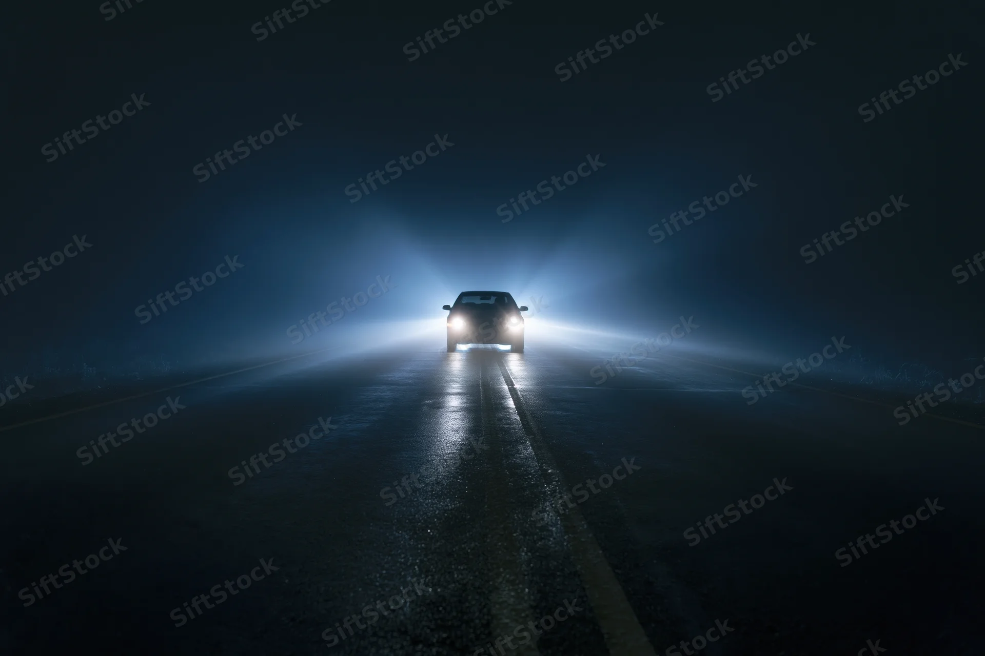 Dark sedan driving toward camera on empty two-lane road at night with headlights on