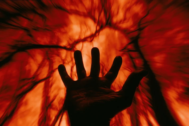 Silhouetted hand reaching upward with fingers spread against a fiery red glowing background