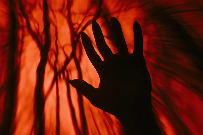 Silhouetted hand reaching upward with fingers spread against a red glowing background