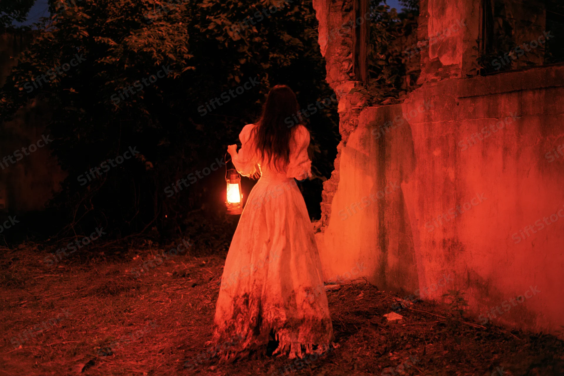 Woman in tattered victorian gown holding lantern walking through overgrown ruins at night
