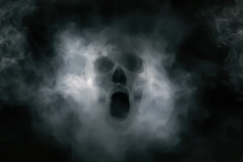Ghostly skull emerging from swirling smoke and fog in dark atmosphere