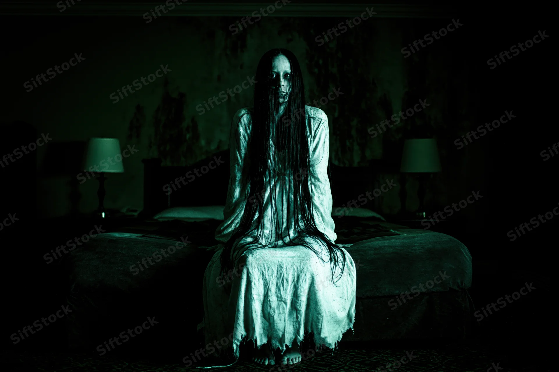 Ghostly woman with long dark hair sitting on bed in dimly lit bedroom