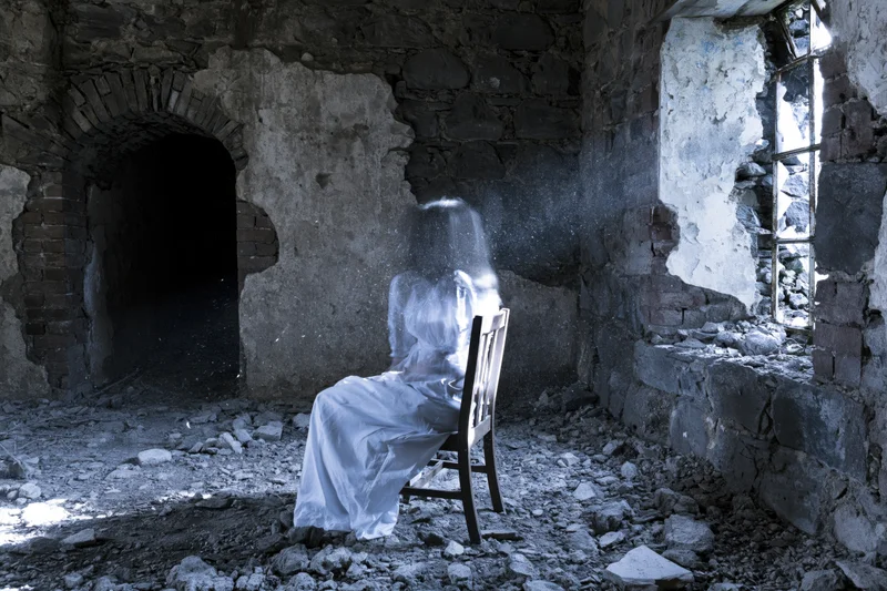 Translucent ghost figure seated on wooden chair in abandoned stone ruin