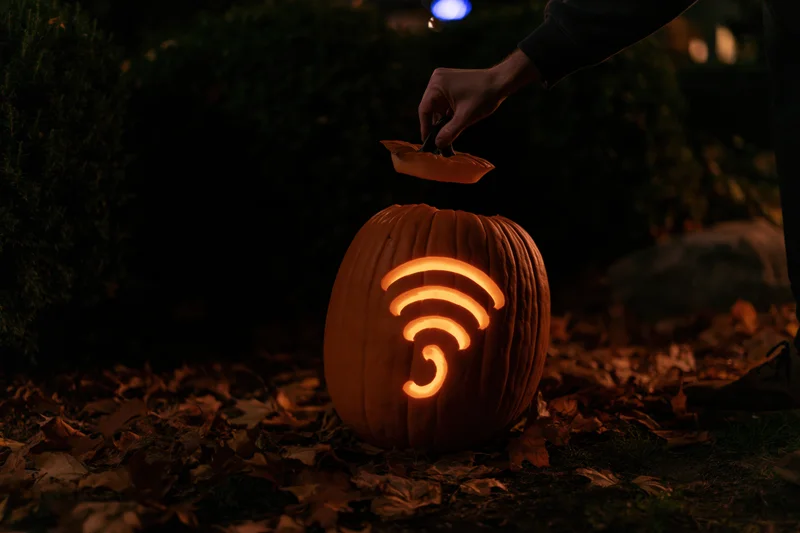 Hand lifting stem lid off glowing jack-o-lantern carved with wifi symbol in garden at night