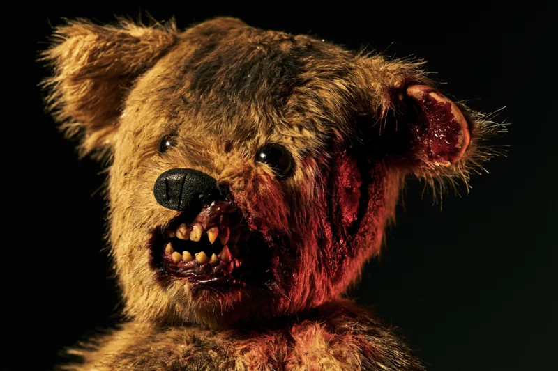 Horror-themed teddy bear with torn mouth and bloodied fur against black background