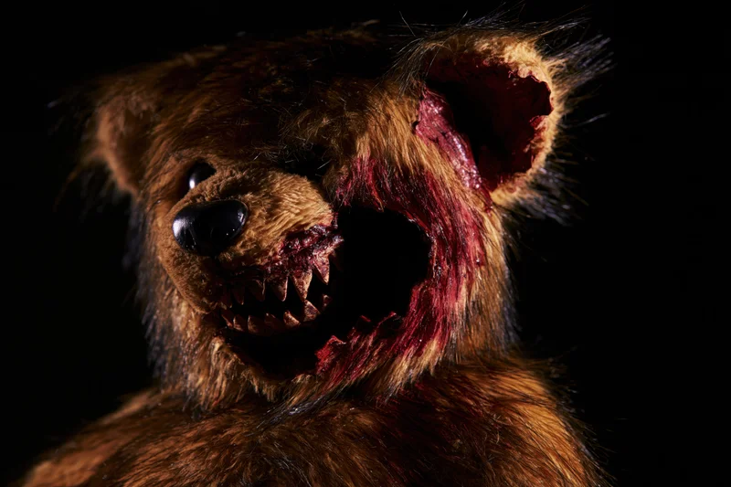 Horror-themed teddy bear with torn mouth and blood on dark background