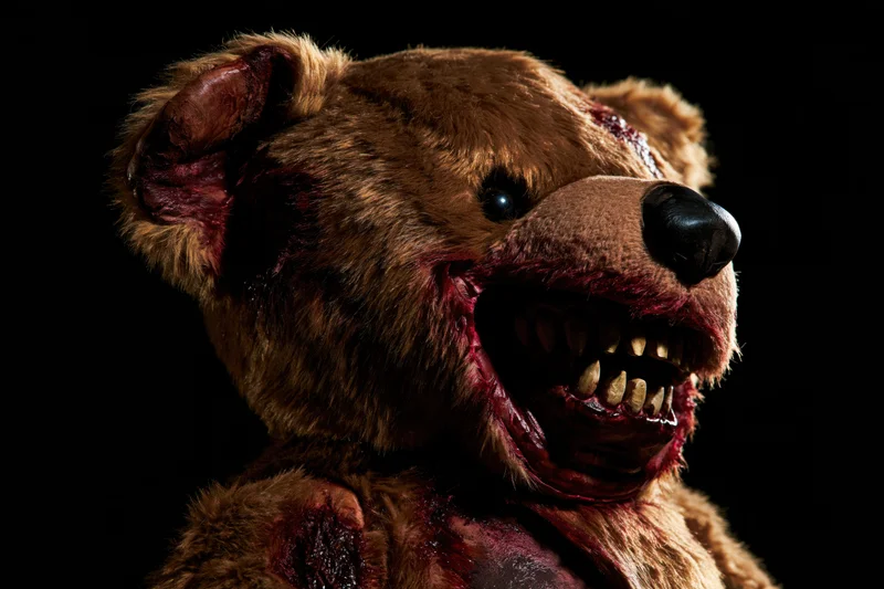 Horror-themed prop teddy bear with grotesque torn mouth and bloodied fur against black background