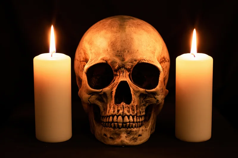 Human skull replica centered between two lit white candles on dark surface