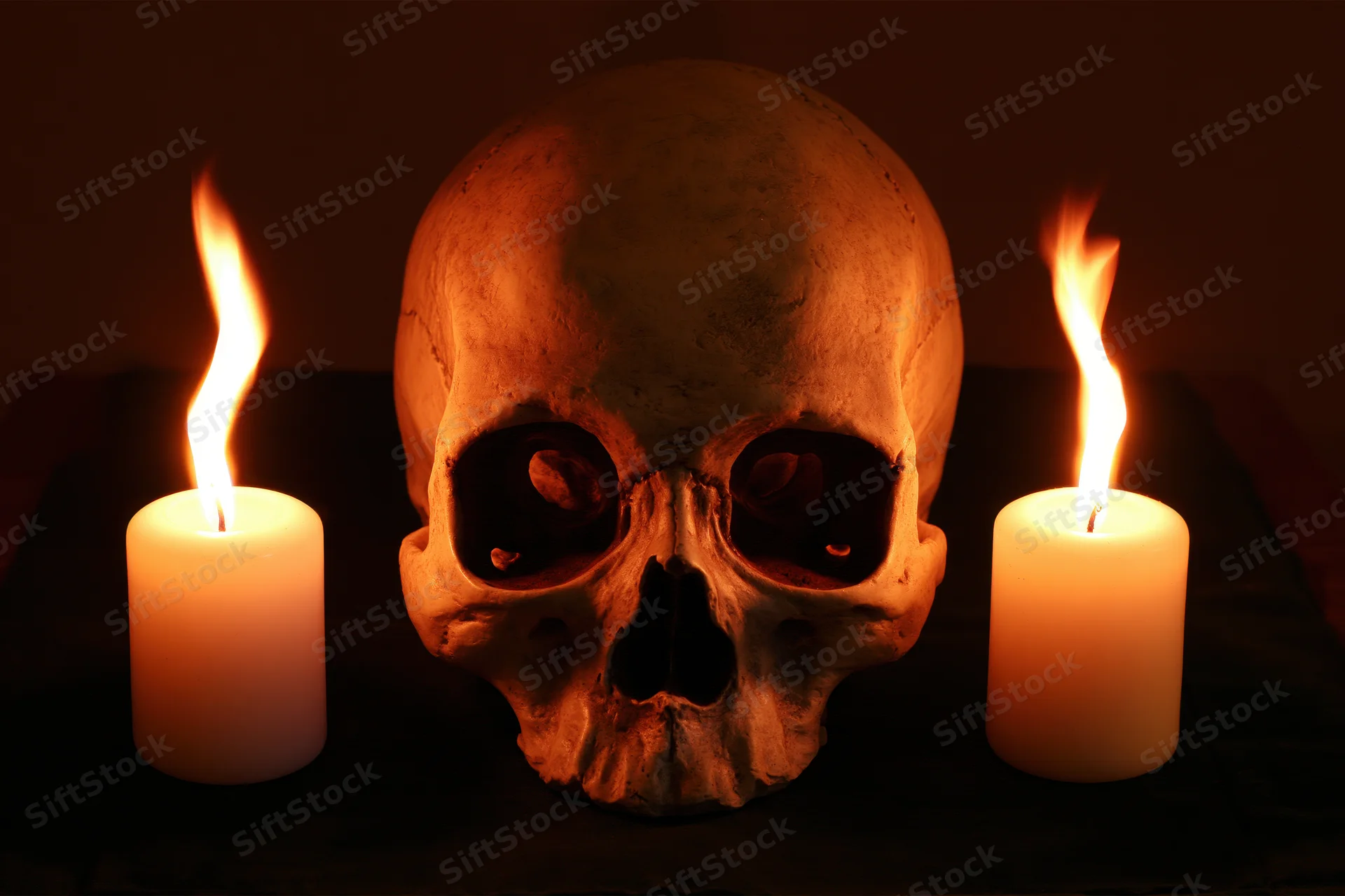 Human skull replica centered between two lit white candles on dark surface