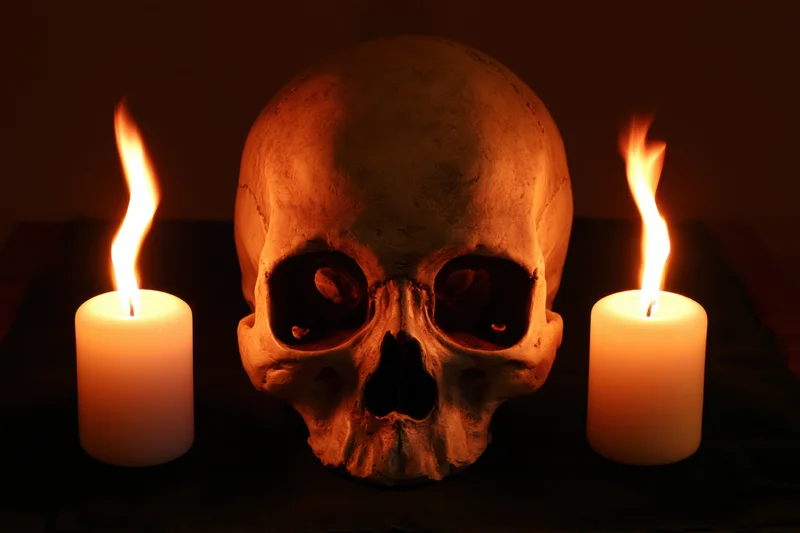 Human skull replica centered between two lit white candles on dark surface