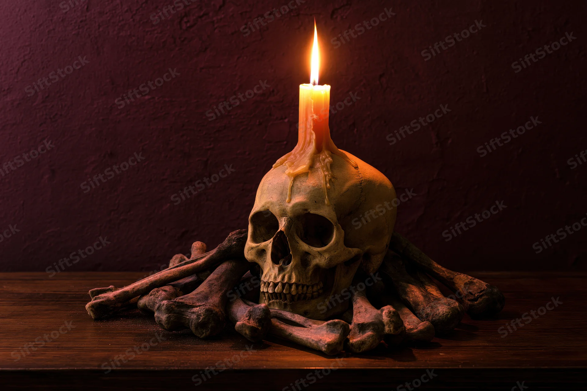 Human skull with lit candle melting on top surrounded by bones on wooden table