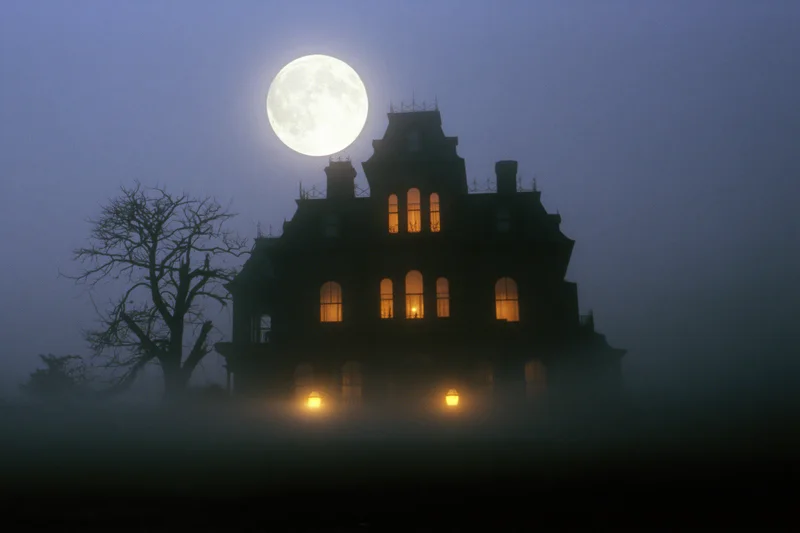 Victorian mansion silhouetted against full moon in fog with glowing windows