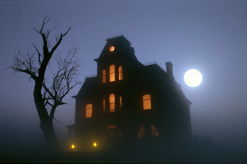 Victorian mansion silhouetted against full moon in fog at night