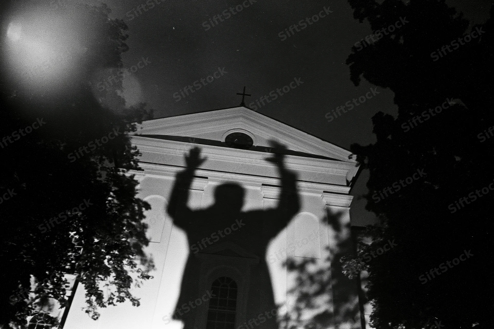 Shadow of a person with arms raised projected onto the facade of a church at night