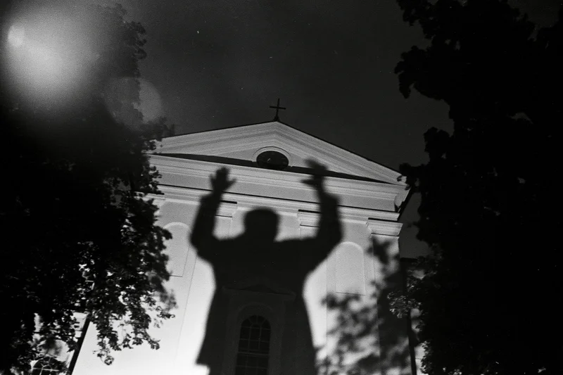 Shadow of a person with arms raised projected onto the facade of a church at night