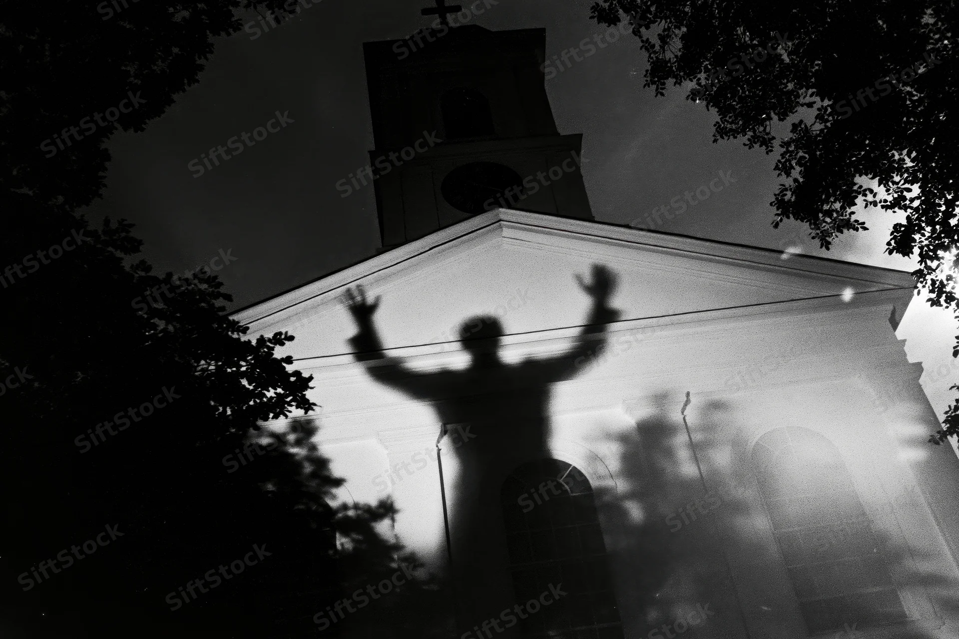 Shadow of a person with arms raised projected onto the facade of a church at night