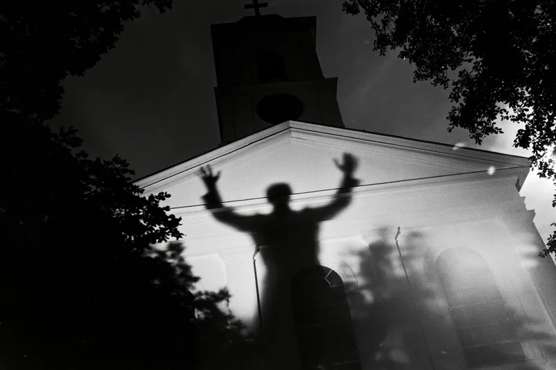 Shadow of a person with arms raised projected onto the facade of a church at night