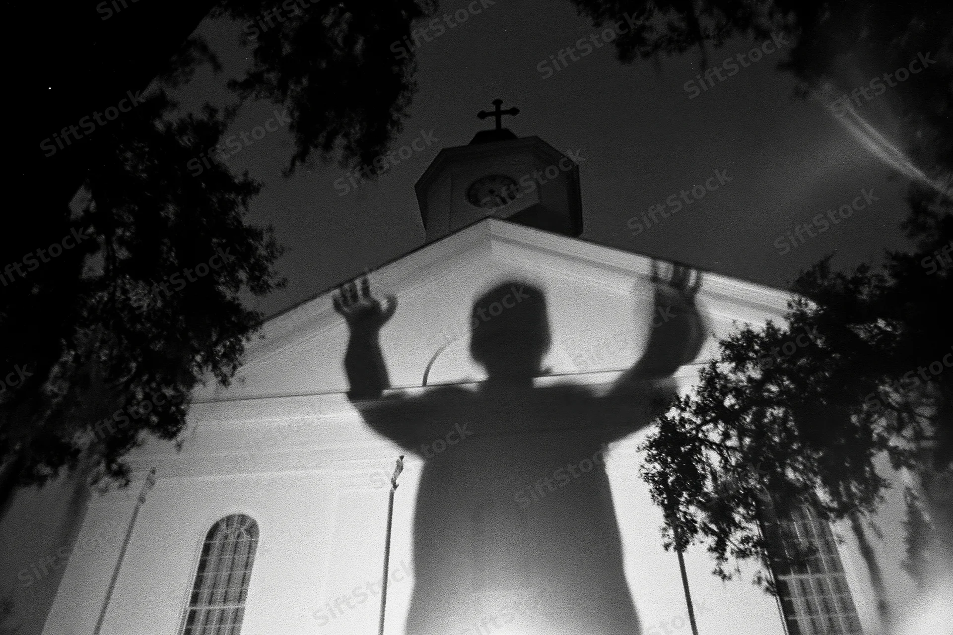 Shadow of a person with arms raised projected onto the facade of a church at night