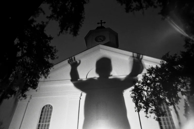 Shadow of a person with arms raised projected onto the facade of a church at night