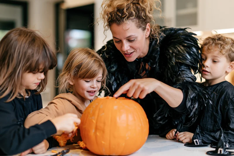 Mother and three children carving a large orange pumpkin at kitchen table