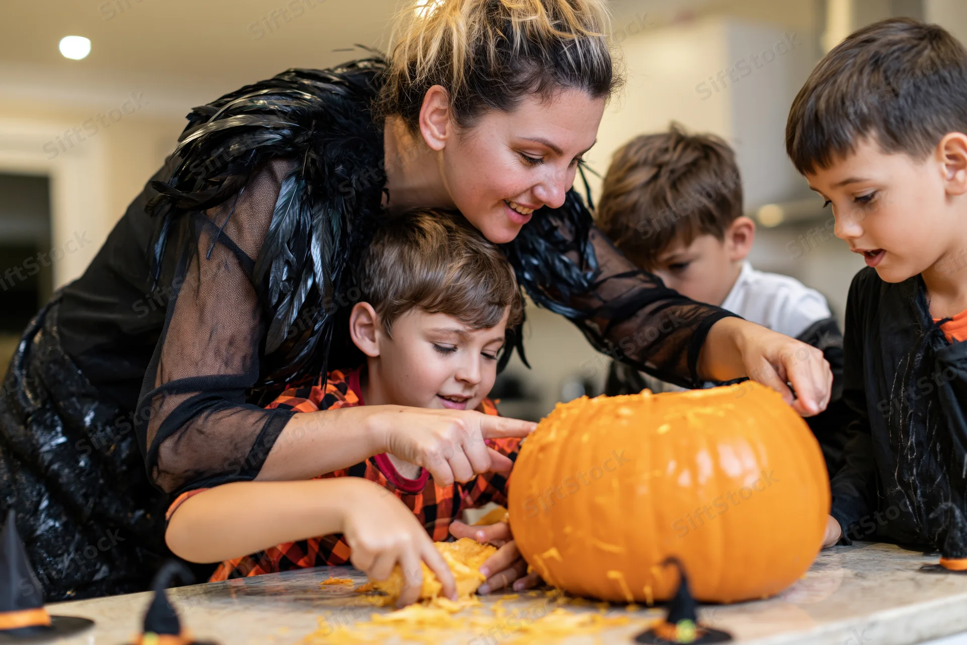 Mother and three children carving a large orange pumpkin at home kitchen table