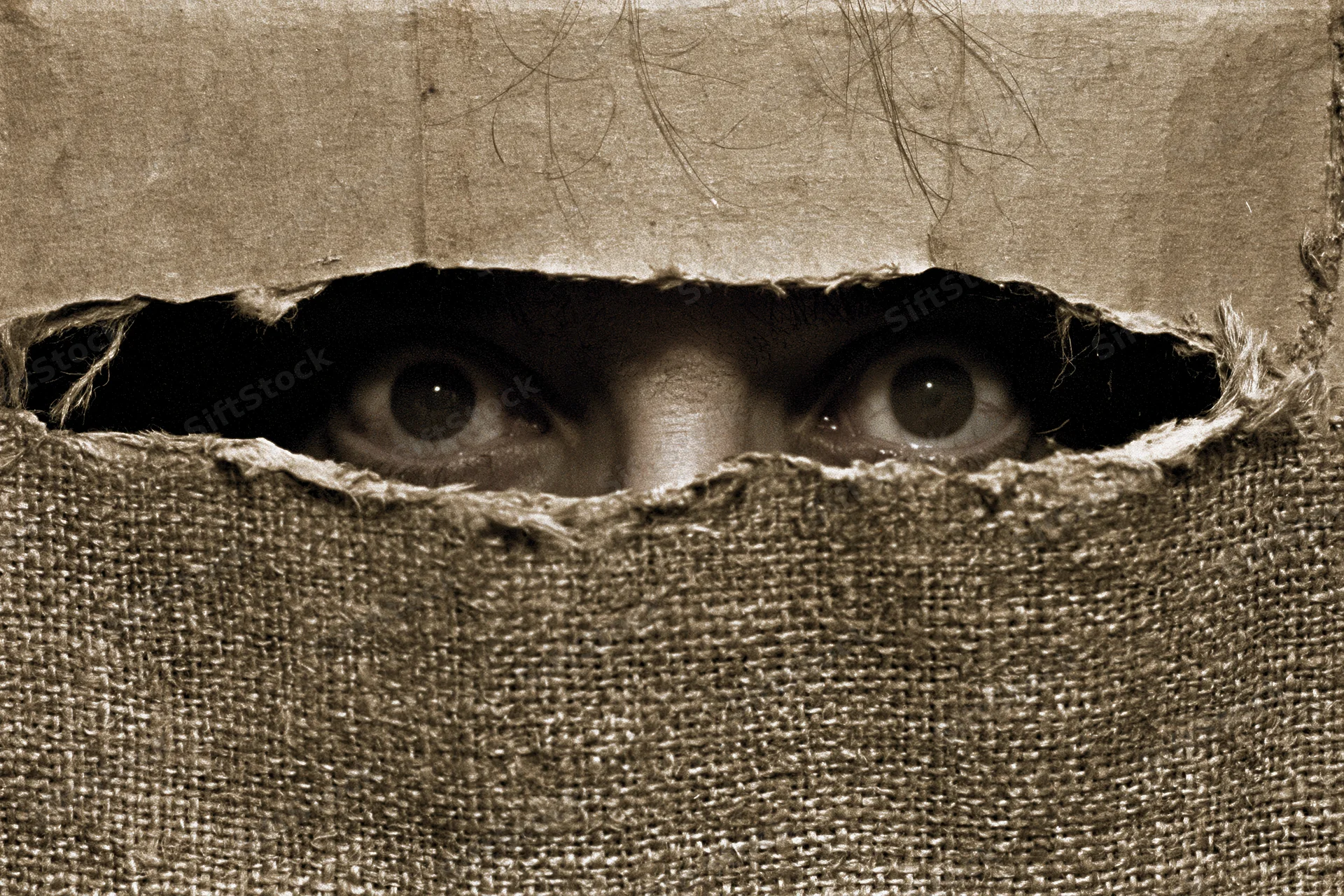 Woman’s eyes staring through a torn burlap hole