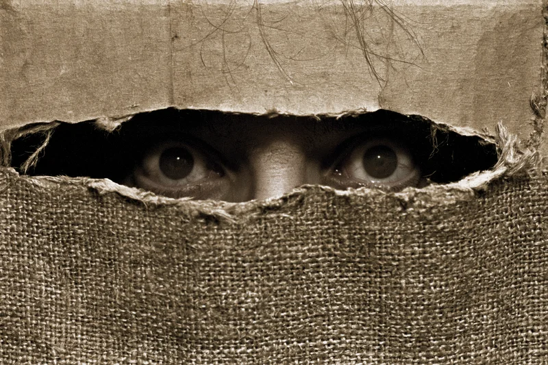 Woman’s eyes staring through a torn burlap hole