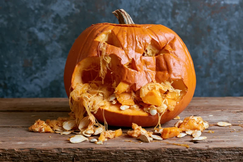 Smashed jack-o-lantern with exposed seeds and pulp on a wooden table
