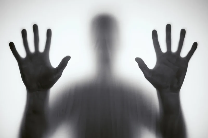 Blurred silhouette of a person pressing hands against frosted glass