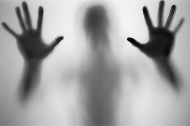 Silhouette of a person pressing hands against frosted glass