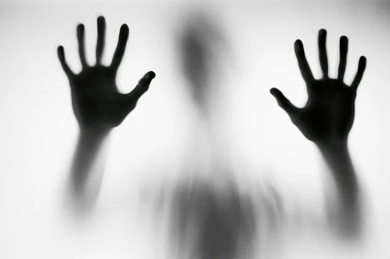 Silhouette of a person pressing hands against frosted glass