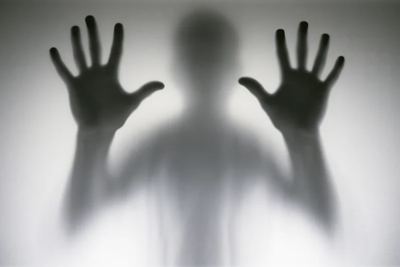 Blurred silhouette of a person pressing hands against frosted glass
