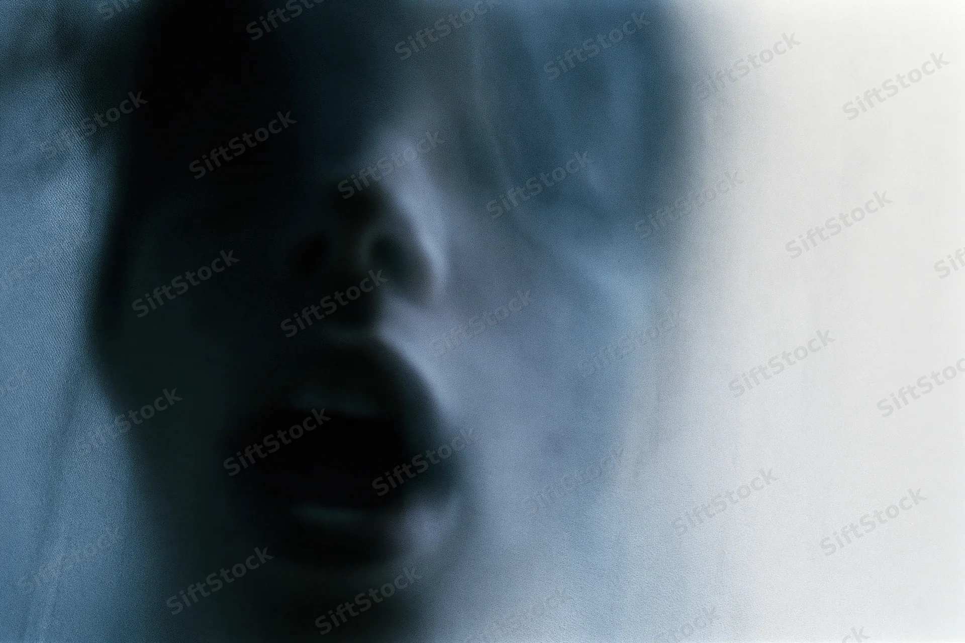 Blurred closeup of a person's face pressed against frosted glass with open mouth and distorted features