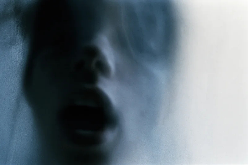 Blurred closeup of a person's face pressed against frosted glass with open mouth and distorted features
