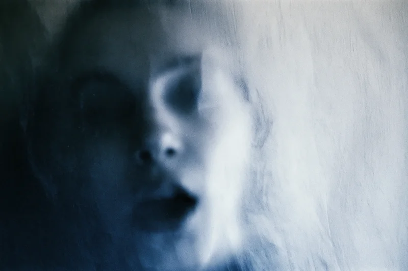 Woman's face pressed against frosted glass with blurred features and blue lighting