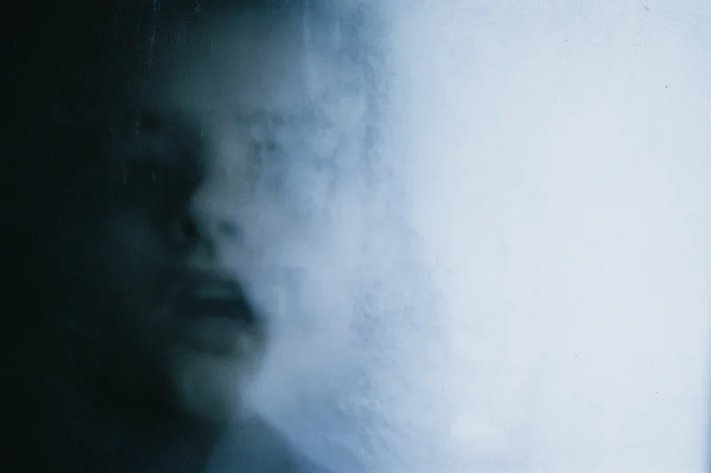 Blurred face pressed against frosted glass in dim indoor light