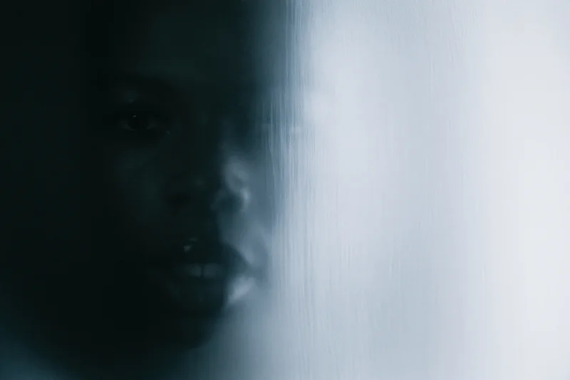 Woman pressing face against frosted glass in dim light