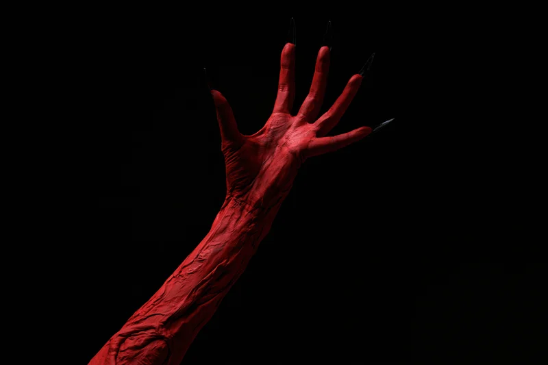 Red-painted demon hand and forearm reaching upward against black background