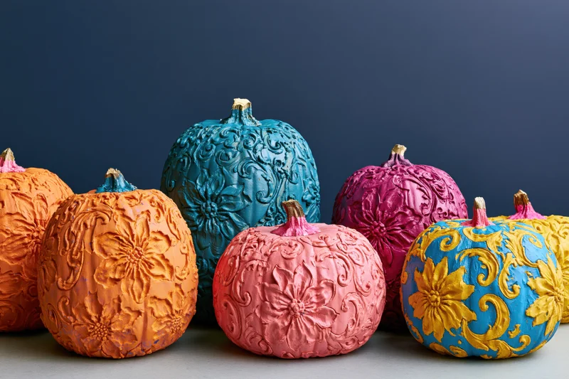 Row of intricately carved and painted pumpkins in vibrant colors arranged on a gray surface against a dark blue background