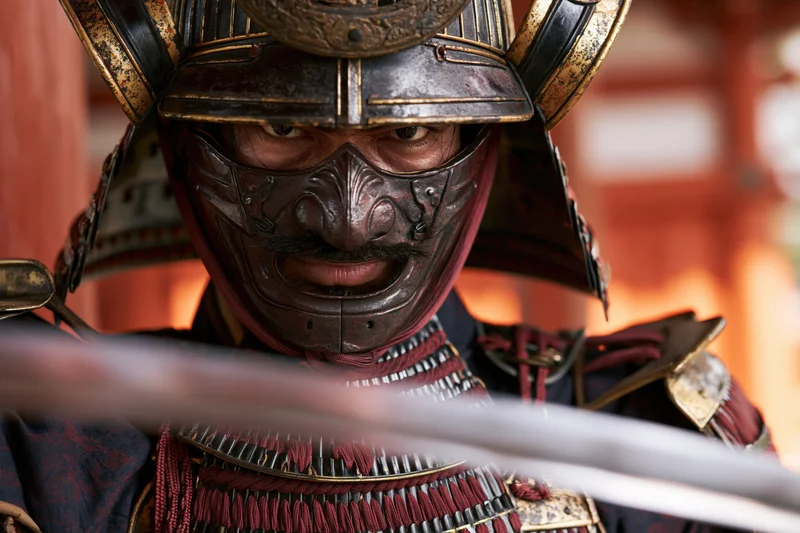 Samurai warrior in full traditional armor staring intensely with sword blade in foreground