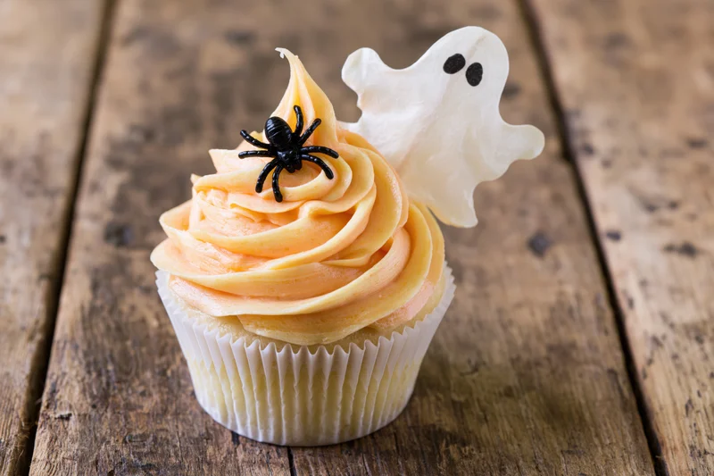 Halloween cupcake with orange buttercream swirl and ghost and spider decorations on wooden table