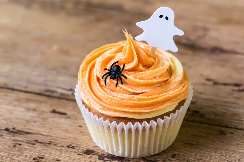 Halloween cupcake with orange buttercream frosting and ghost topper on wooden surface