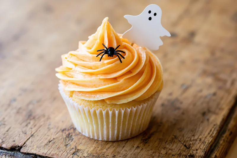 Halloween cupcake with orange buttercream swirl and ghost and spider toppers on wooden surface