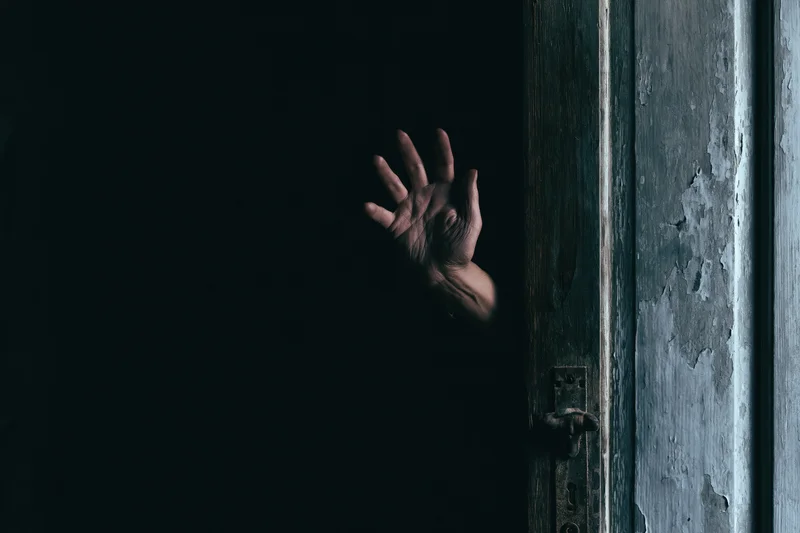 Pale hand reaching from dark behind old weathered door