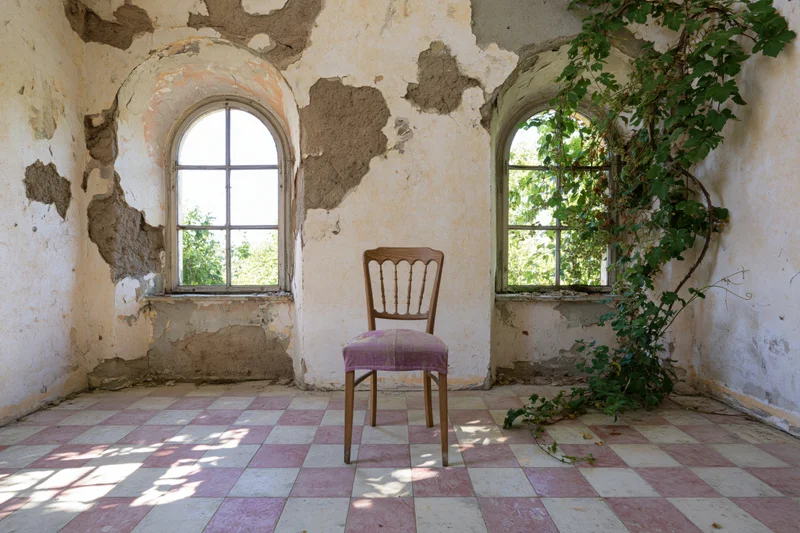 Wooden chair with faded purple seat centered in an abandoned room with arched windows and checkered tile floor