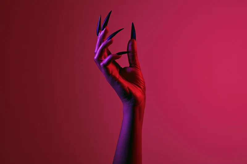 Slender hand with long sharp black nails raised against a red and purple gradient background