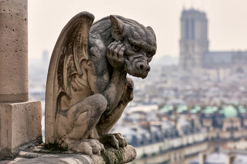 Stone gargoyle sculpture perched on cathedral ledge overlooking paris cityscape